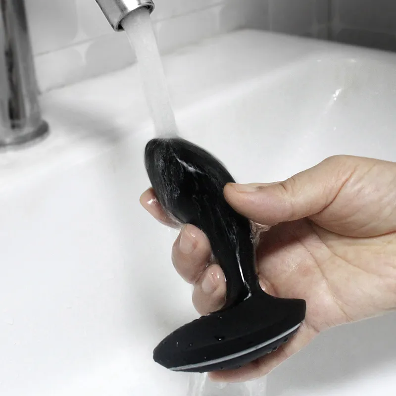 BoomPro electric shock butt plug being rinsed under a faucet, showcasing its easy-to-clean, waterproof design for safe and hygienic use.